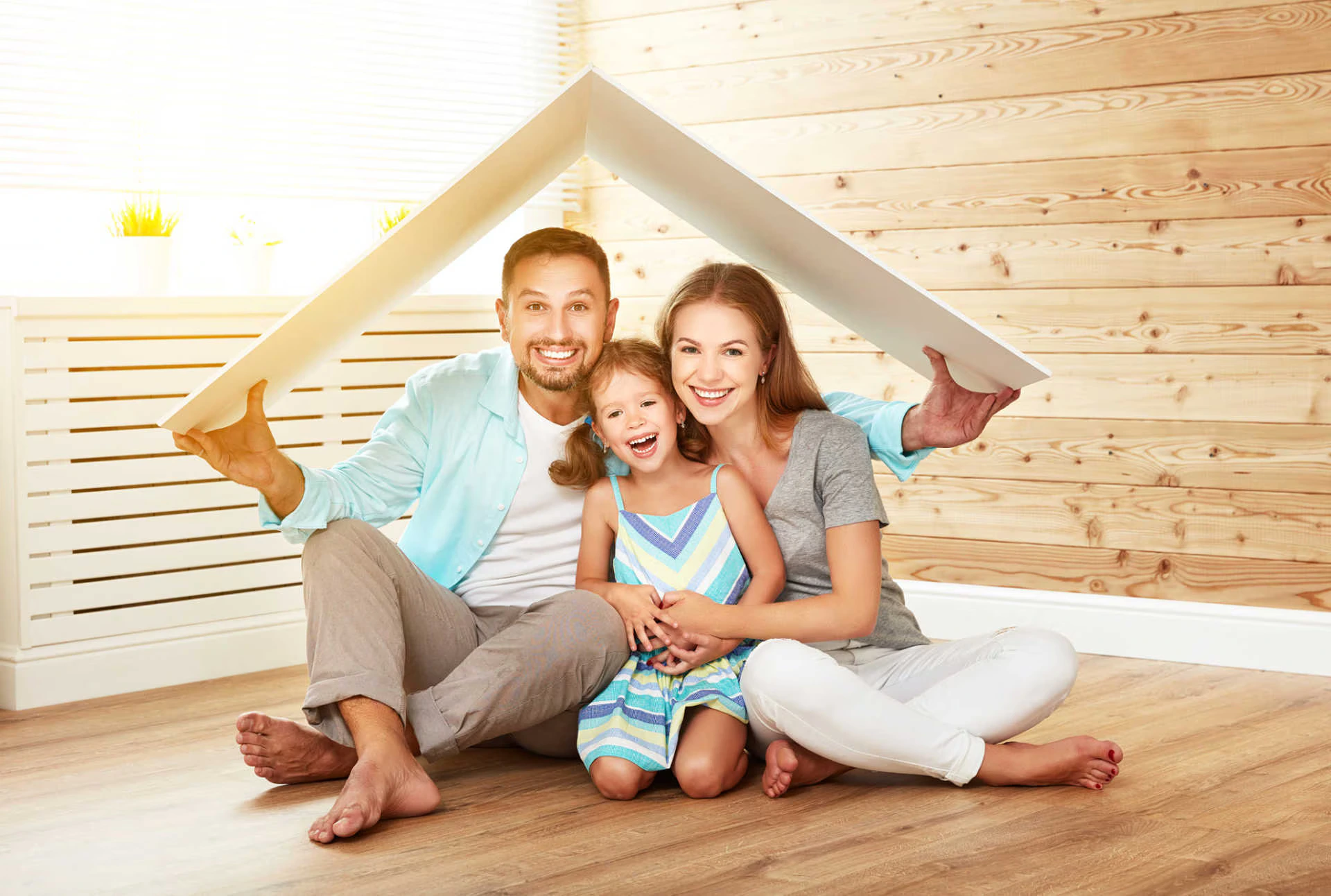 Familia sonriendo en la sala mientras sostiene un techo de cartón sobre sus cabezas