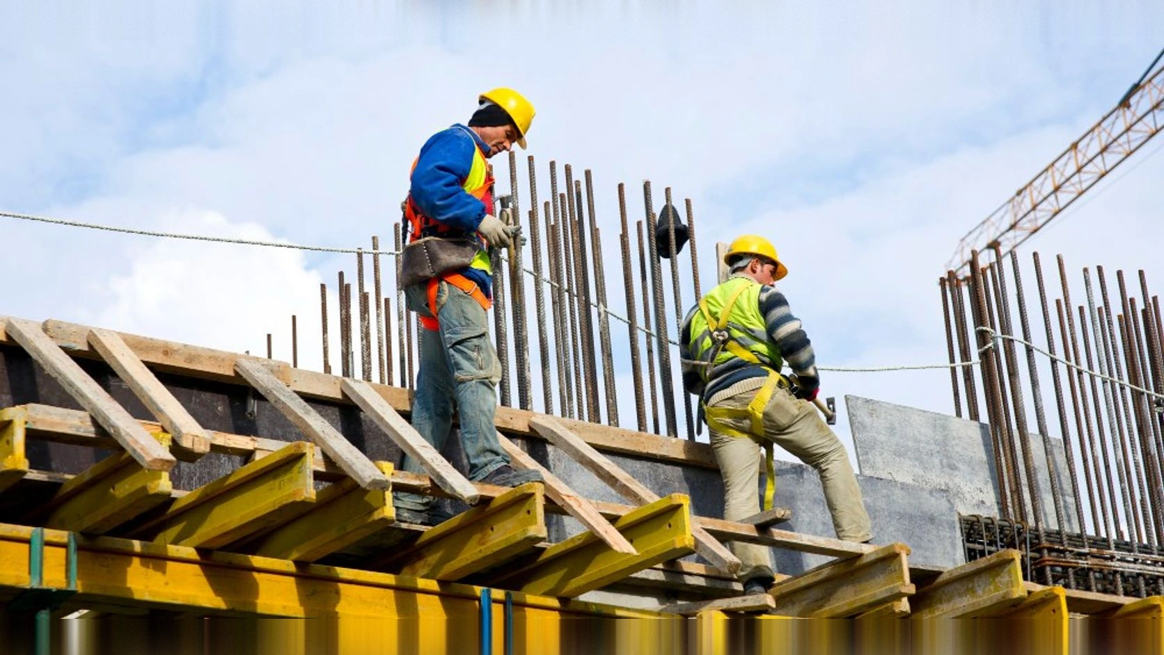 Dos trabajadores con casco y arnés sobre una estructura en construcción