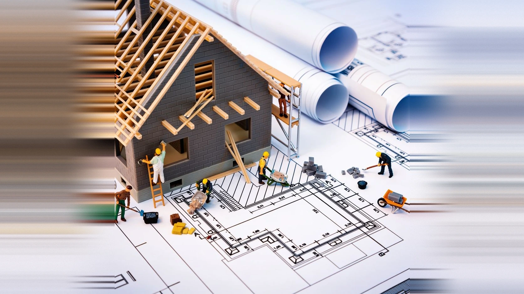 Maqueta de una vivienda en construcción sobre planos enrollados