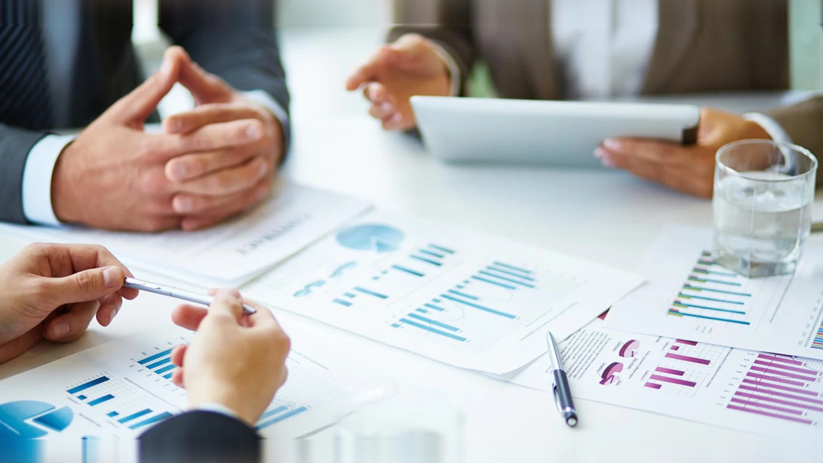 Manos sobre informes financieros con gráficas en una mesa de reunión